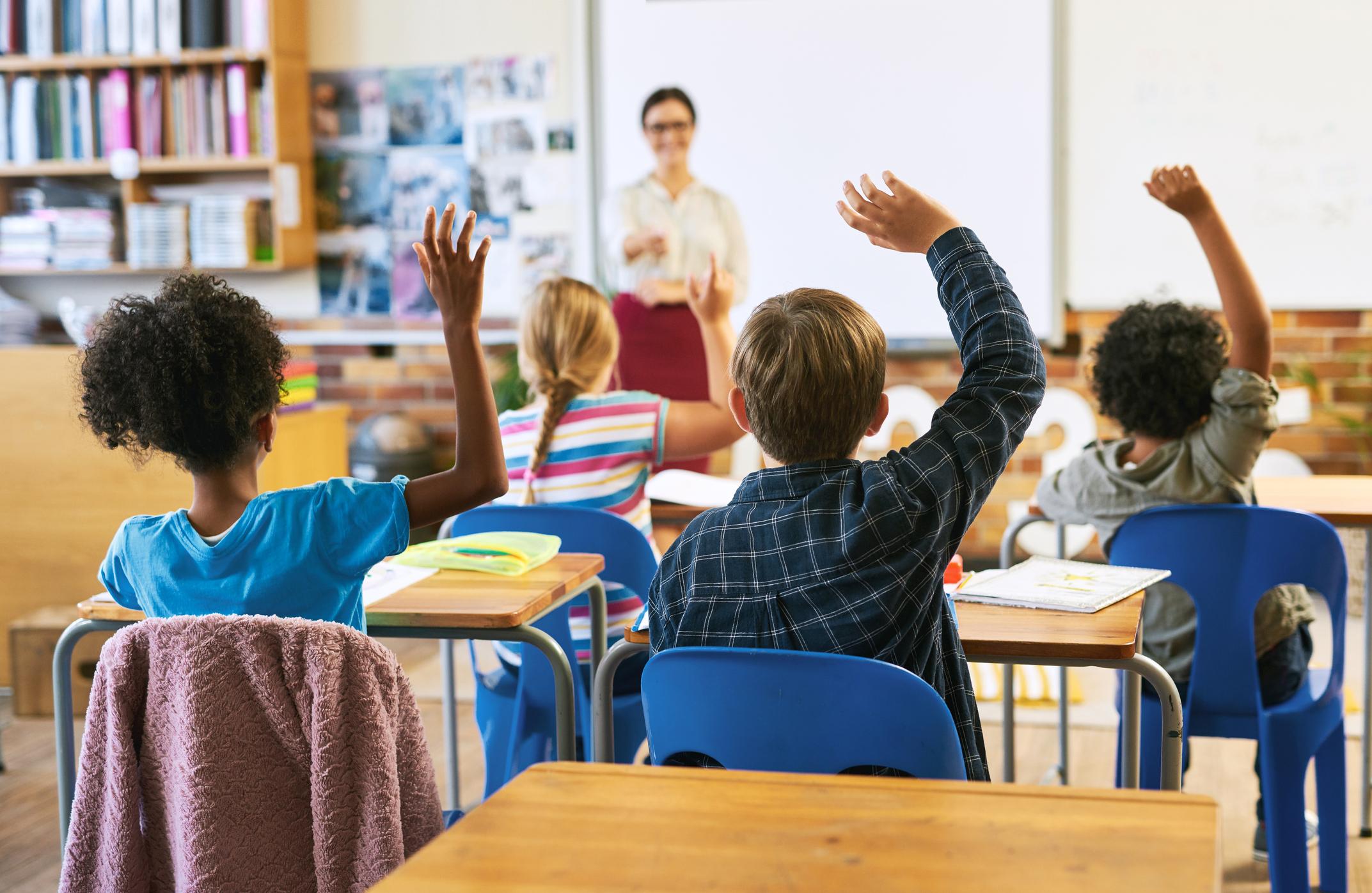 Children raising hands in a classroom at school